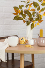 Autumn home decoration. Vase with autumn leaves, glasses of tea, cookies on wooden table and white background.