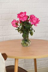 Vase with roses on round wooden table on white bricks background.