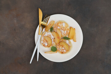 Cottage cheese pancakes with peach and mint leaves on a white plate on a brown background.