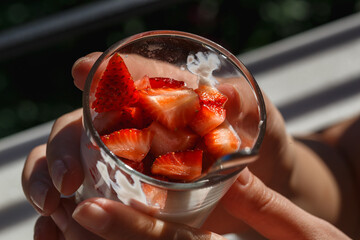 Strawberry custard dessert, yogurt in a glass with fresh strawberry on a hands. Direct sunlight