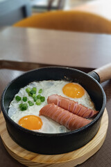 Scrambled eggs in a frying pan with fried meat sausages