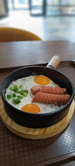 Scrambled eggs in a frying pan with fried meat sausages