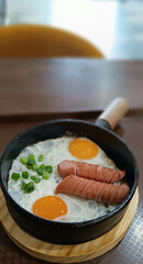 Scrambled eggs in a frying pan with fried meat sausages