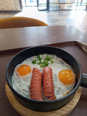 Scrambled eggs in a frying pan with fried meat sausages
