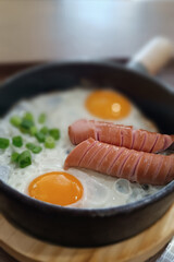 Scrambled eggs in a frying pan with fried meat sausages