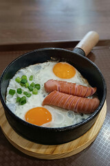 Scrambled eggs in a frying pan with fried meat sausages