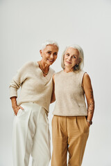 mature ladies in stylish pastel attire posing with hands in pockets on grey, vanity fair style