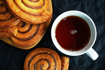 Cup of tea next to cinnamon rolls on dark background