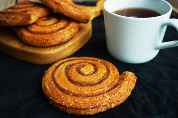 Cup of tea next to cinnamon rolls on dark background