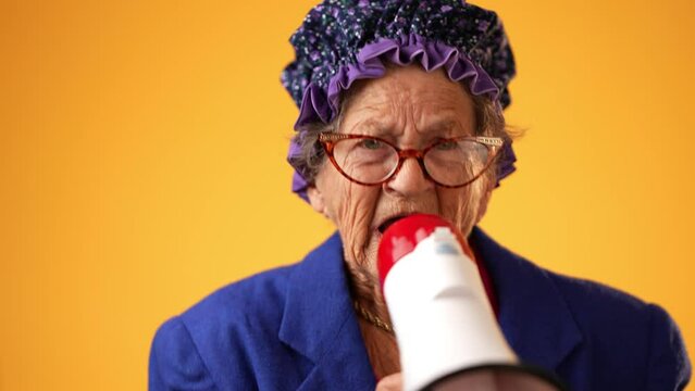 Closeup portrait of funny toothless old elderly senior crazy grandmother woman yelling into megaphone bullhorn announcing something isolated on yellow background.