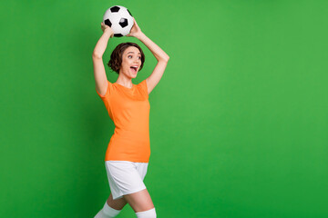 Fototapeta na wymiar Profile portrait of astonished person arms hold ball above head open mouth look empty space isolated on green color background