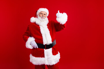 Photo of good mood satisfied man santa claus demonstrate thumb up chrismas new year offer empty space isolated on red color background