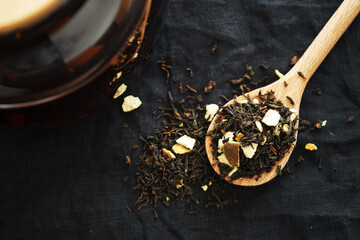 Black tea with pieces of fruit on a wooden spoon next to the teapot on a dark background