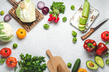 Fresh various vegetables with wooden cutting boards and knife on white kitchen table top view. Cooking vegetarian meal from healthy ingredients, diet food and nutrition concept