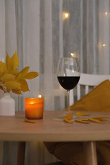 autumn home decoration. Vase autumn yellow leafes, glass of red wine, candle on round wooden table.