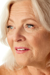 Close-up of beautiful woman in her 60s with natural, healthy skin posing against white studio background. Concept of natural beauty, aging process, elderly beauty, cosmetology, skincare