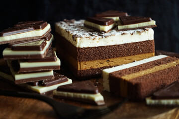 Chocolate cake next to pieces of chocolate on a wooden stand on a dark background