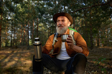 Happy smiling relaxed mature hiker drinking hot tea during hiking outside