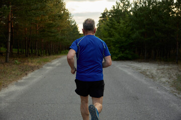 Back view of senior man jogger performing exercise outside among countryside road