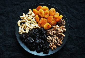 Dried apricots, prunes, nuts on a black plate on a dark background