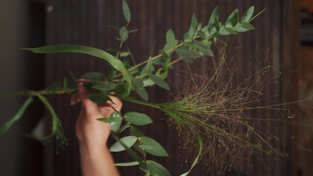 Florist holds a bouquet of panicum and eucalyptus leaves on a wooden background.