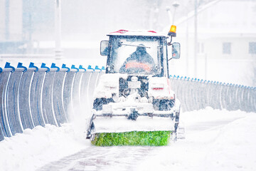 Tractor sweeping snow, clearing snowy sidewalk on bridge in the city during blizzard. Snow plow...