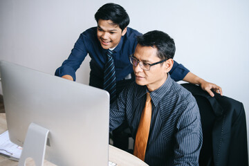 Fototapeta premium Confident young Asian businessman working with mature coworker sitting in front of computer at the office.