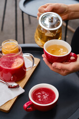 Close-up girl pours tea from a teapot into a cup in a cafe. Healthy drinks, fruits and herbal tea. Vegan, eco products
