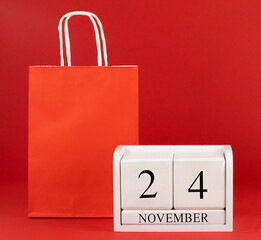 November 24 white wooden calendar and paper bag on a red background close-up. Concept trade, store,...