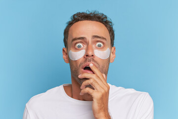 Close-up of guy looking at camera with frightened expression and covering his mouth with his hand,...
