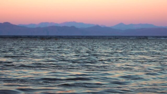 Close up of calm water in the foreground and mountain range on the opposite shore at sunset