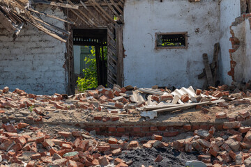 The white walls of an old ruined wooden village house. Broken walls, a ruined roof. Piles of garbage, wooden boards, bricks