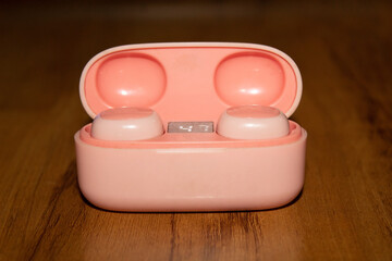Cute pink wireless Airdopes case on a wooden background. Close up.