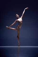 Full-length image of tender, slim, elegant woman, ballerina in beige bodysuit staying on pointe against blue studio background. Concept of classical dance, art and grace, beauty, choreography