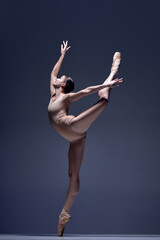 Elegant, attractive woman, professional ballerina in beige bodysuit, standing in pointe against...