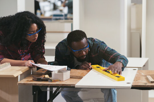 African American male and female carpenter working at wood factory. Two male and female joiner working in wood factory