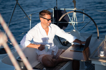 Contented man in sunglasses sitting on a yacht deck with a cup of coffee