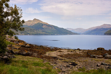 Fototapeta na wymiar From across Loch Goil, a distant view of Carrick Castle with hazy hills in the background
