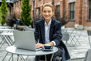 Young pretty business woman sitting at cafe and working on laptop