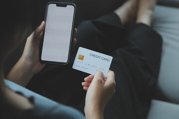 A credit card in the hands of a young businesswoman pays for a business on a mobile phone and on a desk with a laptop.