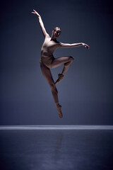 Beautiful, slim, elegant woman, ballerina in motion, posing in beige bodysuit and pointe against blue studio background. Concept of classical dance, art and grace, beauty, choreography, inspiration
