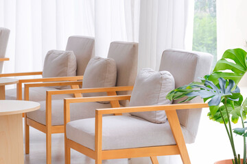 Perspective side view of gray cushions on beige armchairs with round wooden desks near interior glass wall and white curtain inside of modern coffee shop, selective focus © Prapat