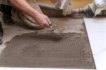 A construction worker applies cement for laying floor ceramic tiles with a spatula. Selective focus
