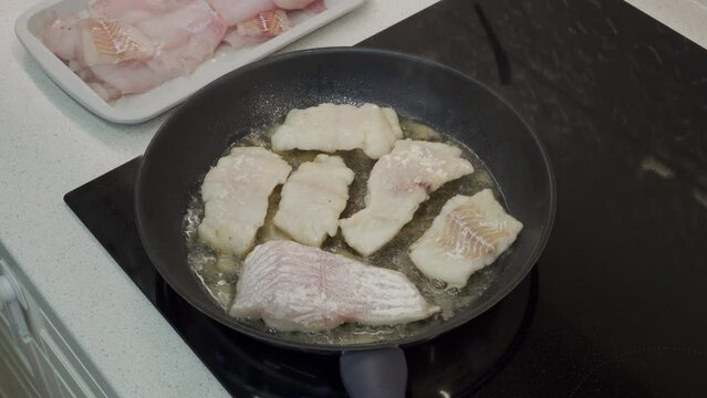 woman frying cod fish in a frying pan in the kitchen at home