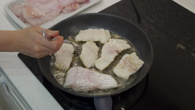woman frying cod fish in a frying pan in the kitchen at home