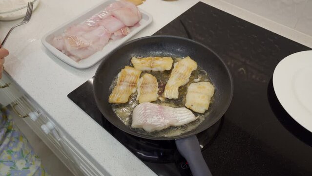 woman frying cod fish in a frying pan in the kitchen at home