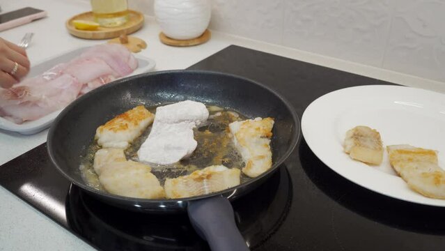woman frying cod fish in a frying pan in the kitchen at home