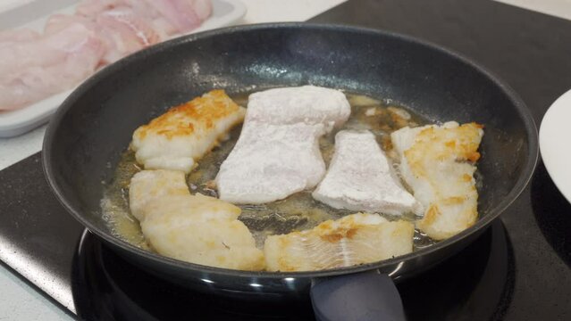 woman frying cod fish in a frying pan in the kitchen at home