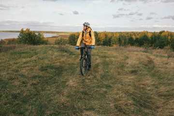  active lifestyle.A cyclist in a protective helmet with a backpack rides a black mountain bike through a coniferous forest in autumn.Mountain Bike