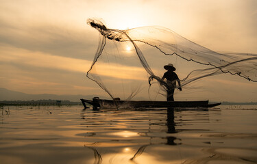 Silhouette of fisherman at sunrise, Standing aboard a rowing boat and casting a net to catch fish for food